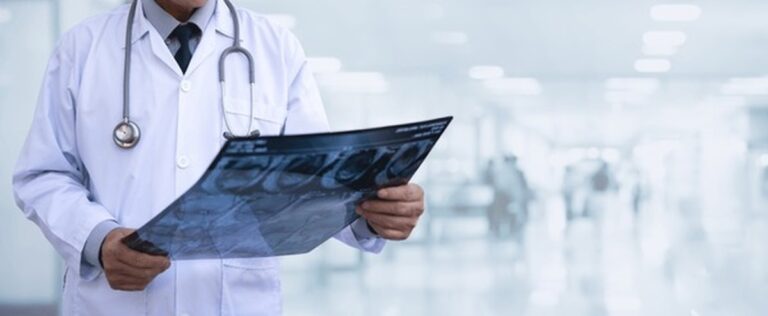 Clinician in a white coat examining an imaging film in a hospital corridor
