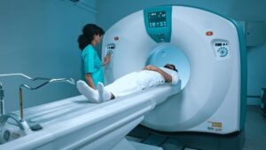 Technologist at the console of a CT scanner while a patient lies positioned on the table